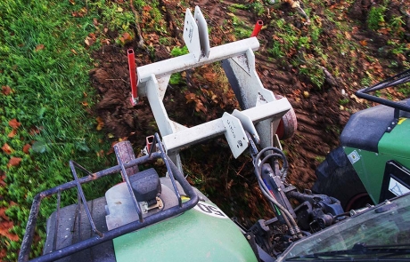Ein Traktor, der von oben gesehen wird, zieht einen weißen Pflug durch ein Feld, wendet den Boden und hinterlässt eine Linie frisch gepflügter Erde neben dem grünen Gras.